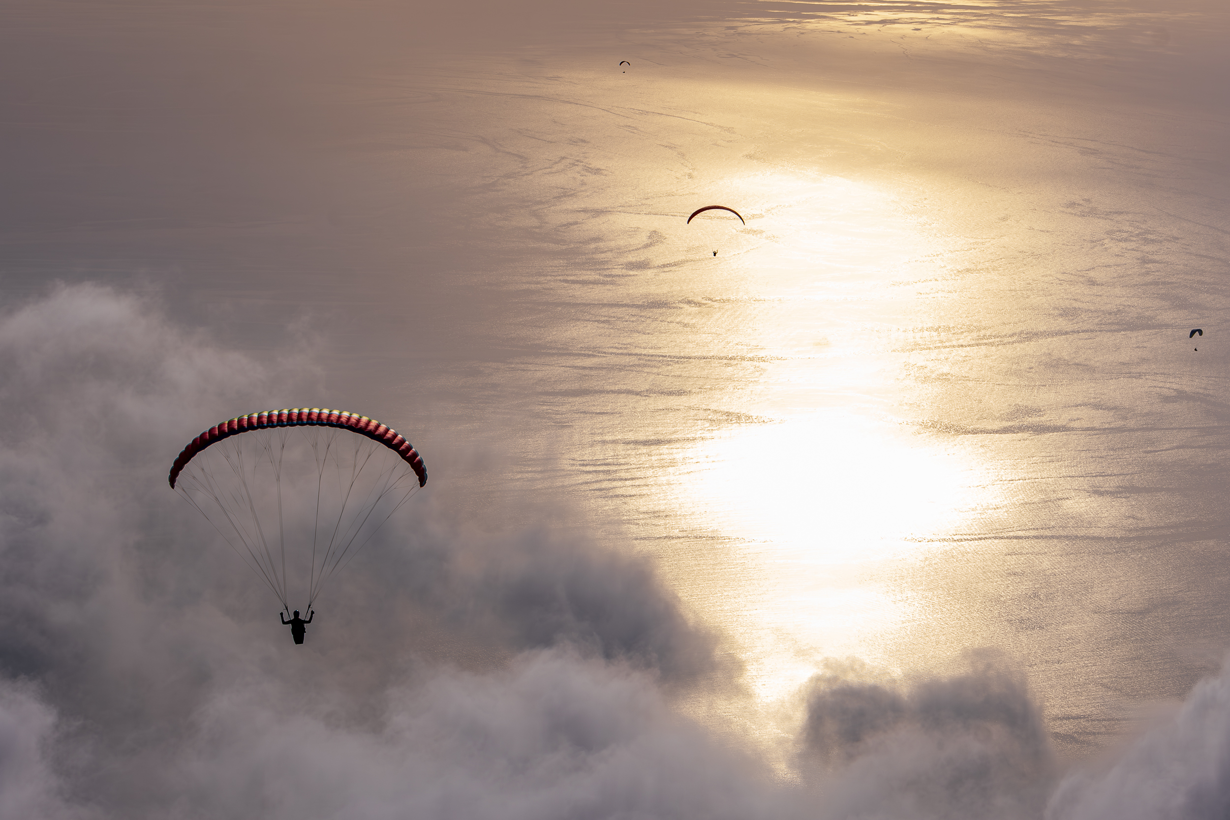 Paragleiter beim Flug in den Wolken über den Bergen mit Blick auf See